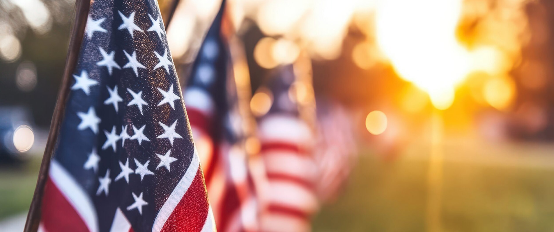 Numerous United States flags bask in the glowing evening sunlight, conveying themes of unity and freedom on a tranquil evening, perfect for memorial occasions.